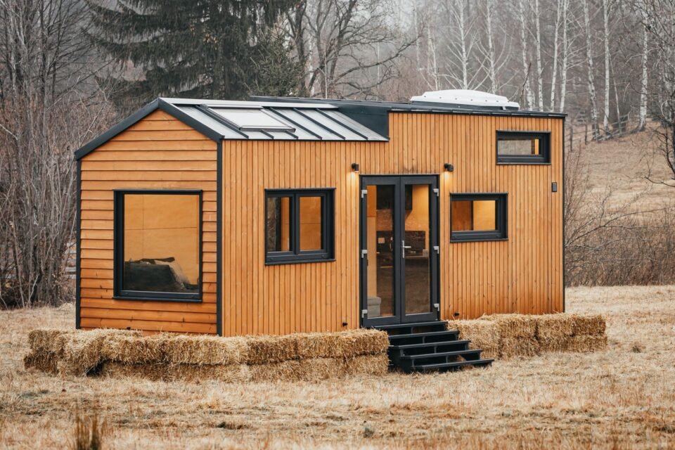 Dřevěný tiny house v přírodě s balíky slámy.