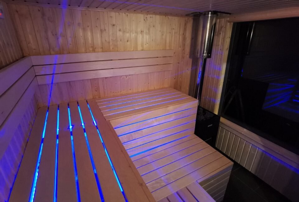 Dřevěná sauna s modrým osvětlením uvnitř místnosti.