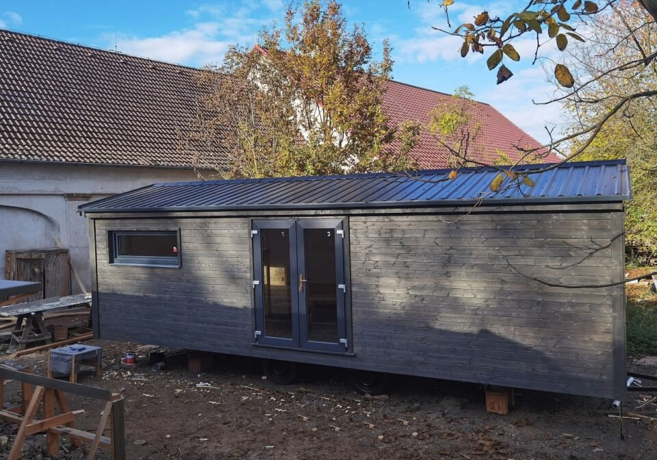 Malý dřevěný domek na kolech vedle domu