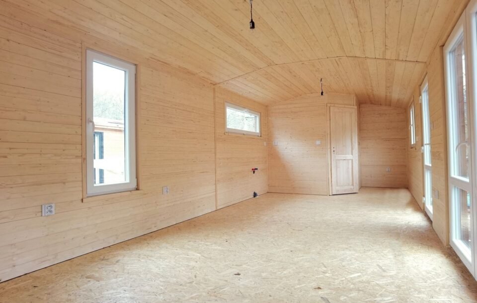 Prázdná dřevěná místnost s okny a dveřmi.