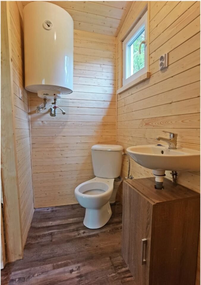 Dřevěná koupelna s WC, umyvadlem a ohřívačem.