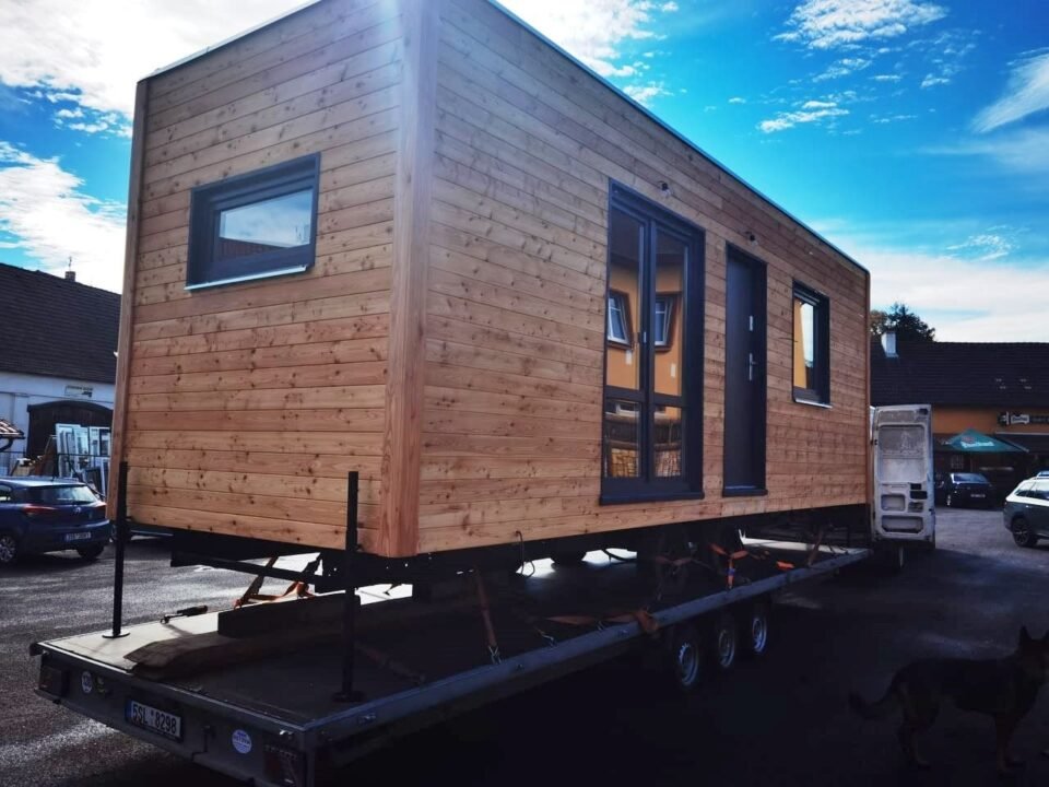 Dřevěný domek na přívěsu na slunném parkovišti.