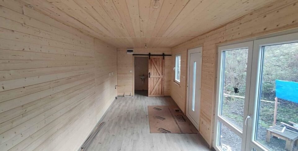 Dřevěný interiér s dveřmi a oknem do zahrady.