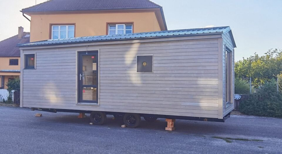 Dřevěný mobilní dům na kolech před domem.