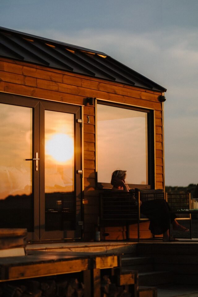 Osoba sed&iacute; před srubem při z&aacute;padu slunce.