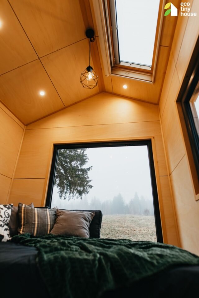 Interi&eacute;r mal&eacute;ho domu s velk&yacute;m oknem a postel&iacute;.